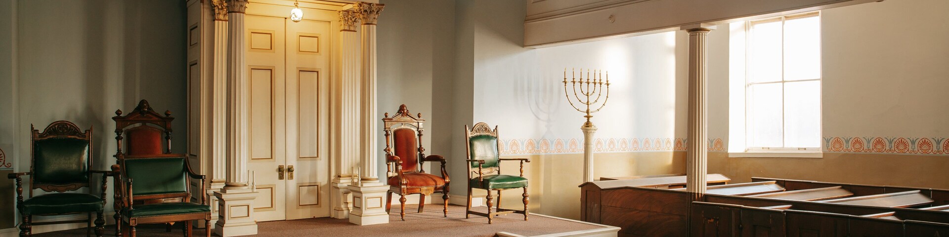 Interior de uma sinagoga com bancos de madeira, um arco para a Torá e um candelabro.