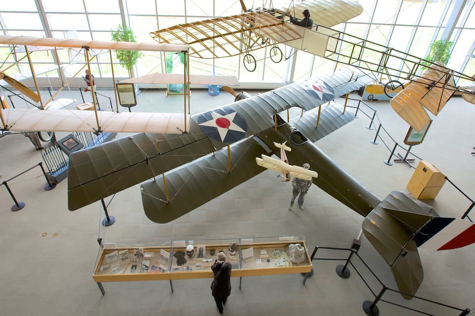 A museum with various aircraft on display, including a large fighter plane and several biplanes.