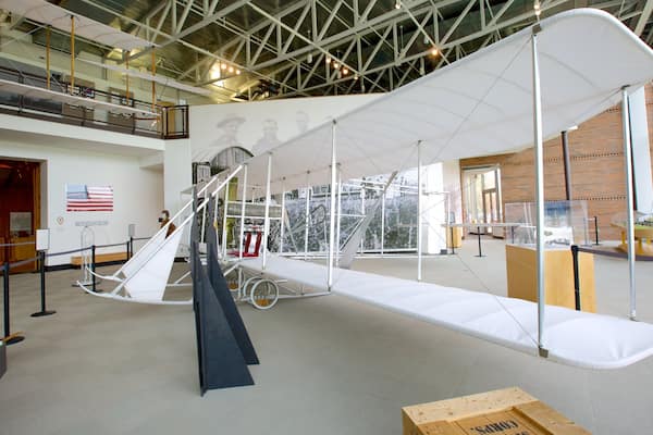 An indoor exhibit with a large biplane model, a staircase, and a display of historical artifacts.