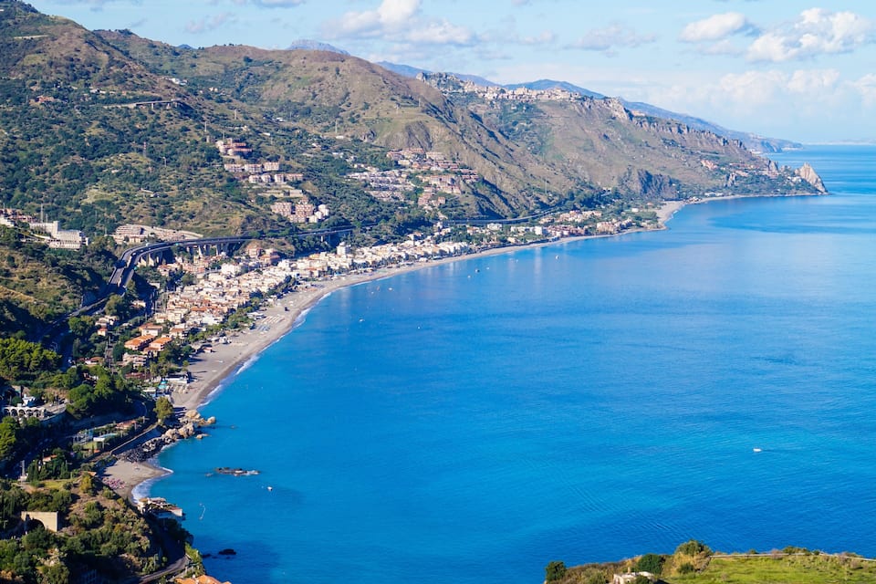 A coastal town with a long beach, a bridge, and mountains in the background.