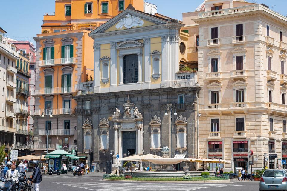 A historic square with ornate buildings, a fountain, and outdoor cafes.