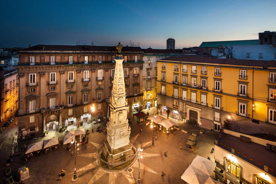 Una plaça històrica amb una torre del rellotge al centre, envoltada de cases tradicionals i zones d'esbarjo a l'aire lliure.