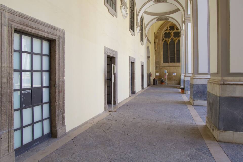 A corridor with arched ceilings, stone columns, and a tiled floor.
