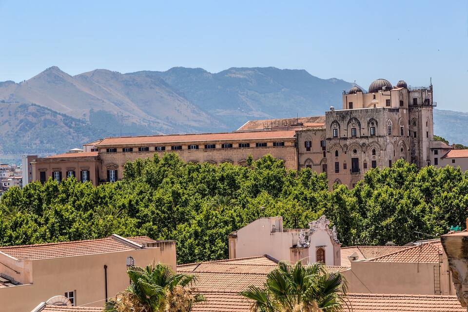 A historic building with a bell tower, surrounded by lush green trees and mountains in the background.