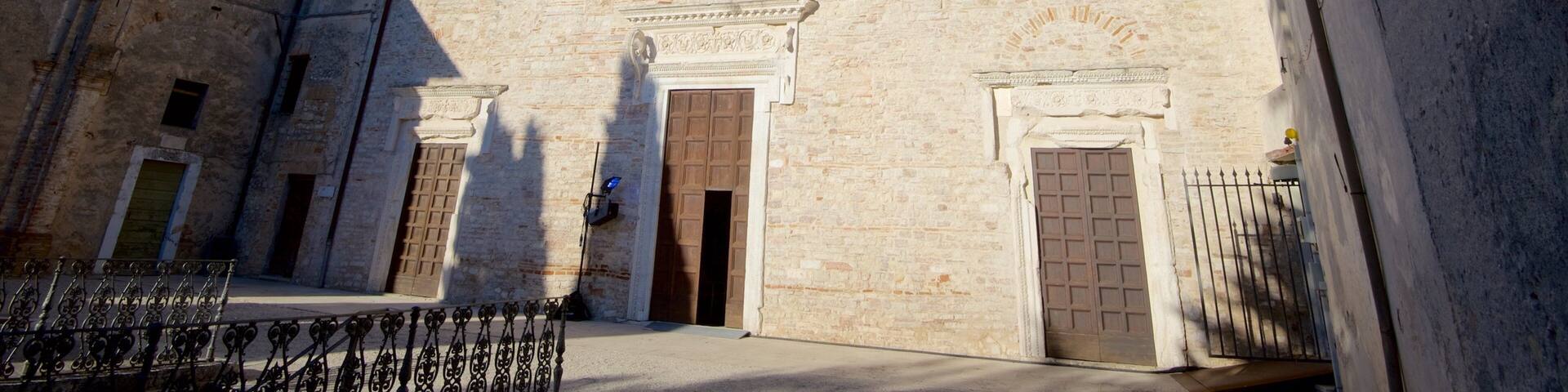 Un edificio histórico de piedra con una torre de campanas, ventanas de arco y un patio.