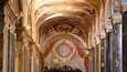 An ornate church interior with detailed frescoes, a large circular stained glass window, and marble columns.