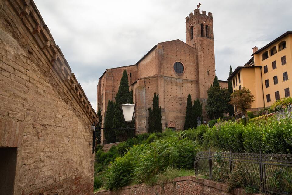 Eine historische Kirche mit einem hohen Glockenturm, umgeben von üppiger Vegetation und traditioneller Bebauung.