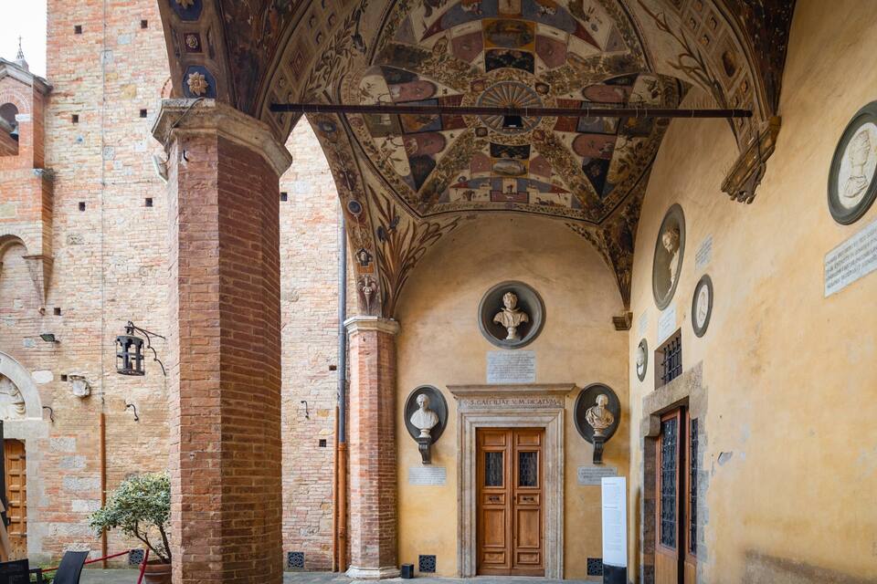 Um corredor ornamentado com porta de madeira, colunas de tijolo e teto com afrescos elaborados.