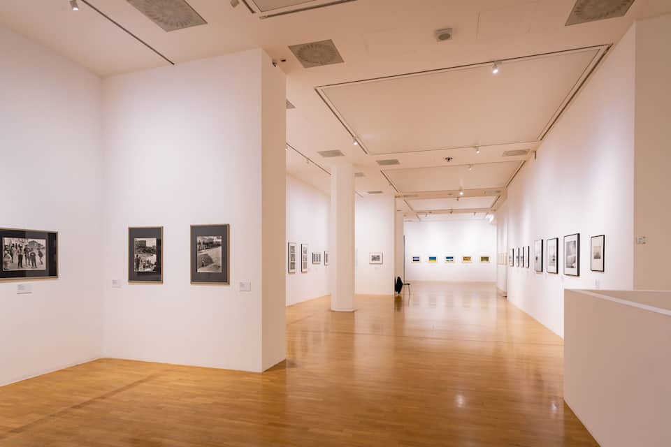 Una galería de arte con pisos de madera y paredes blancas, exhibiendo fotografías enmarcadas.