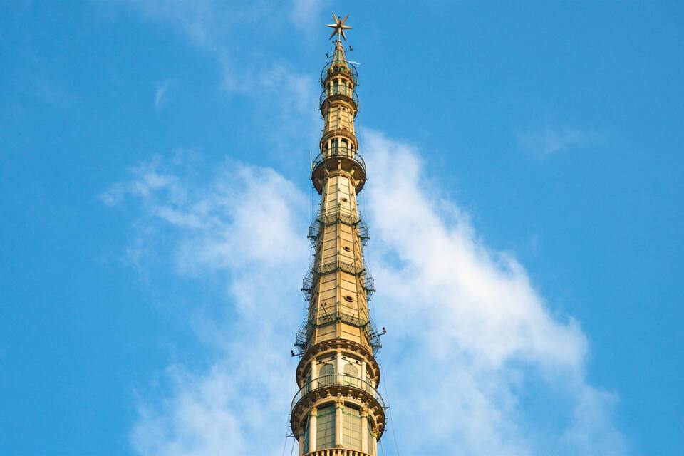 Ein hoher Turm mit einem Stern auf der Spitze vor blauem Himmel.