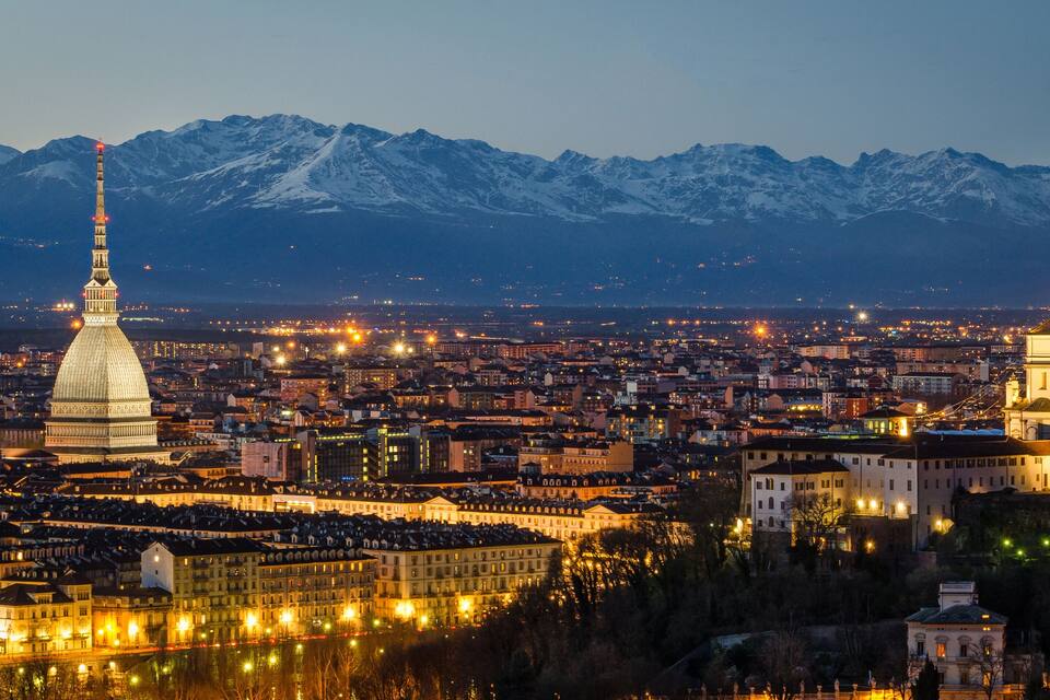 A cityscape with a prominent dome and a tower, set against a backdrop of snow-capped mountains.