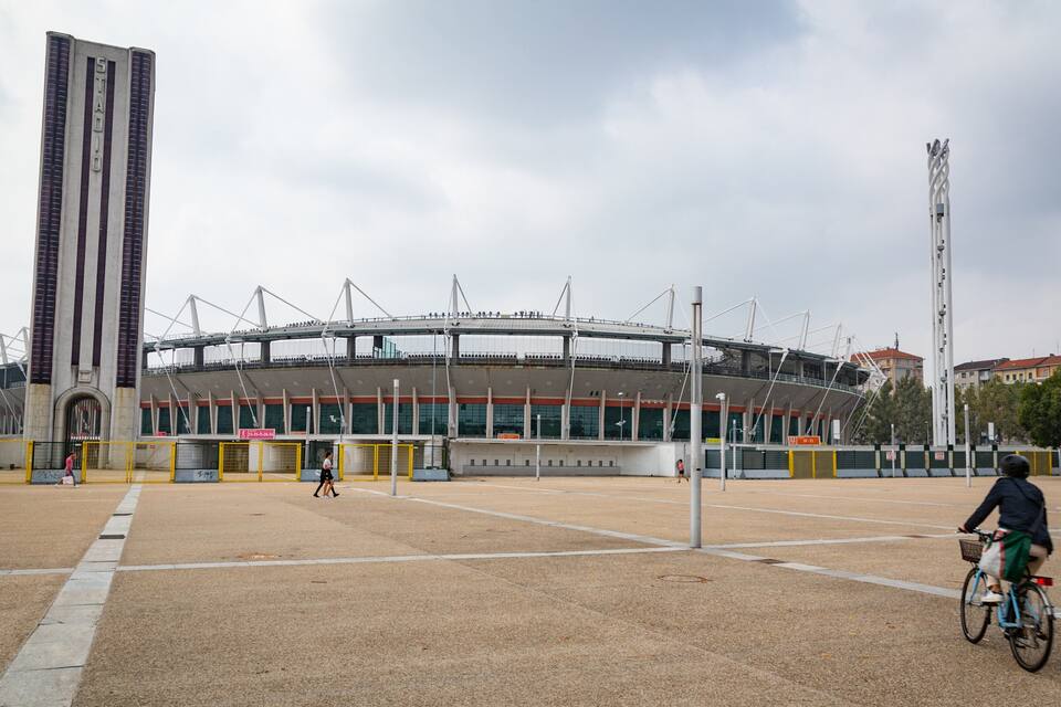 A large stadium with a tall tower and a cyclist in the foreground.