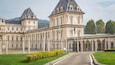 A grand historic building with classical architecture, featuring columns, a large entrance, and flags.