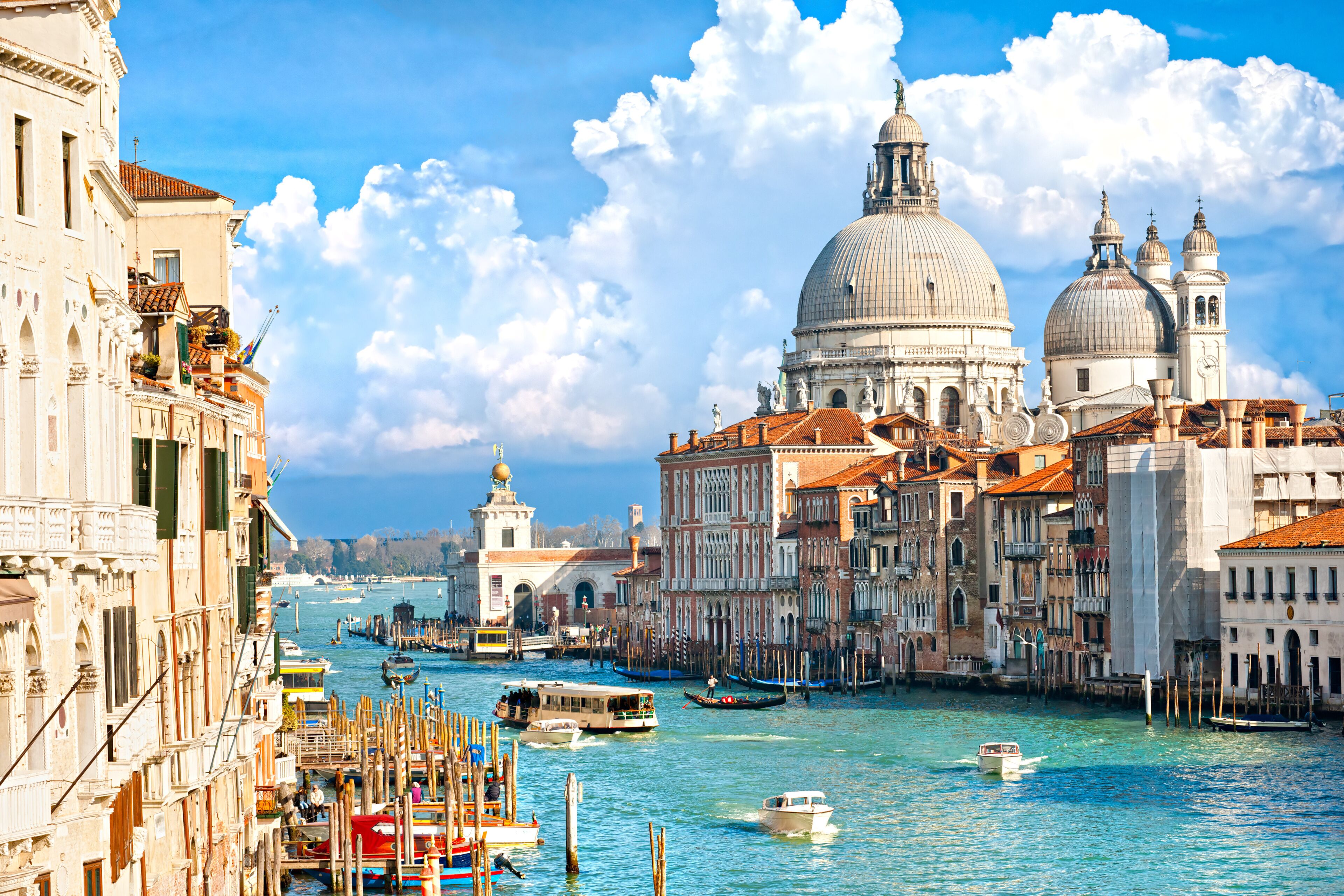 A canal with boats, historic buildings, and a prominent dome structure.