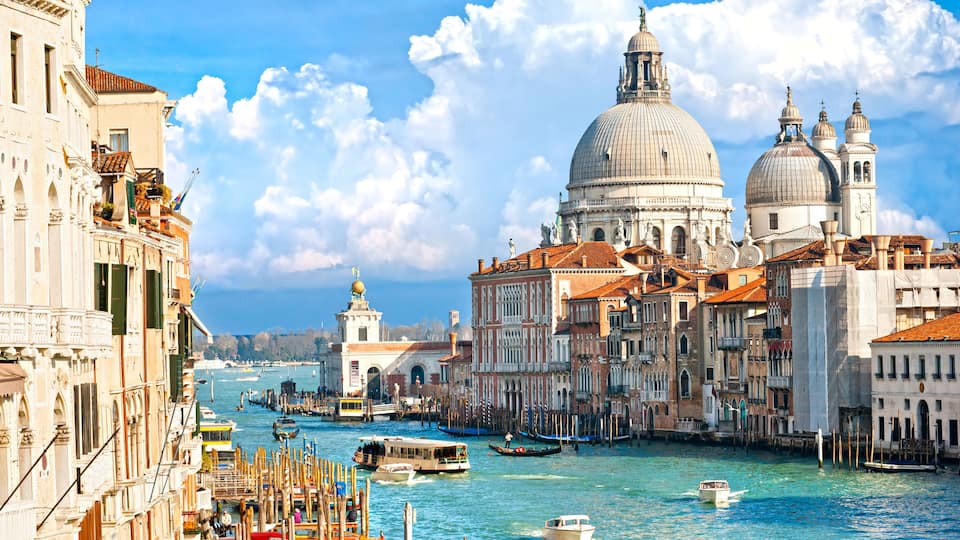 A canal with boats, historic buildings, and a prominent dome structure.