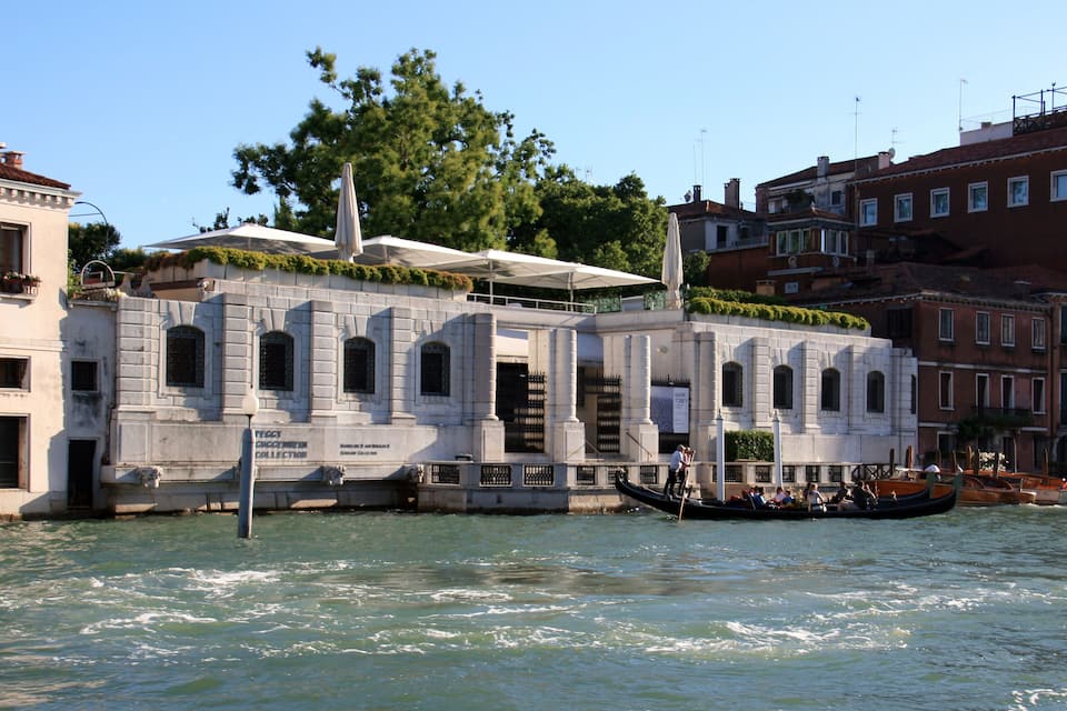 A historic building with a collection sign, gondolas on the water, and a clear sky.