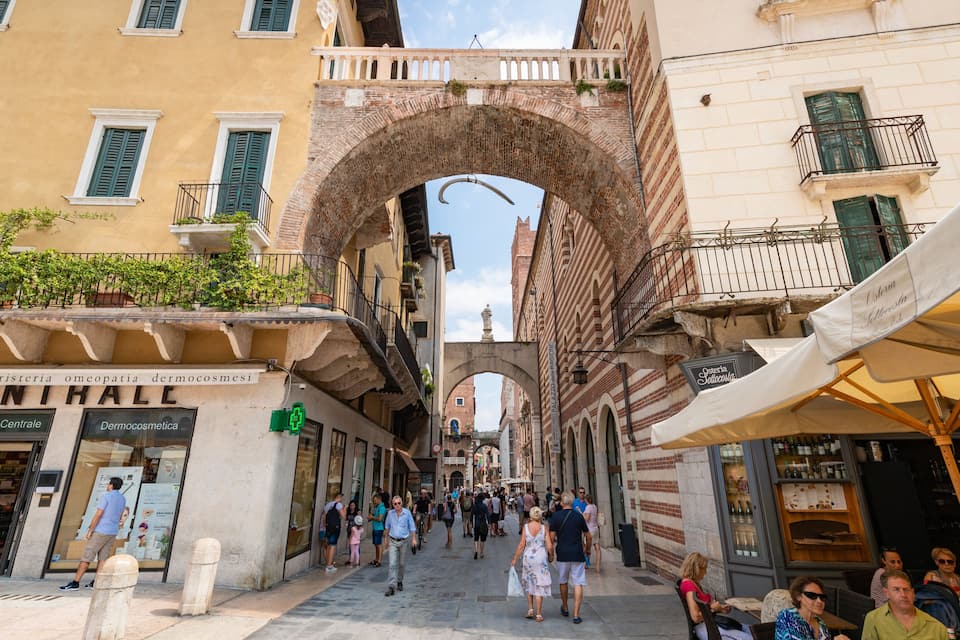A bustling street with a prominent archway, shops, and outdoor seating areas.