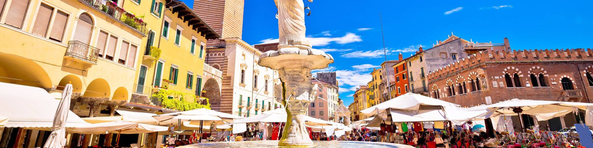 A historic square with a fountain, a clock tower, and market stalls.