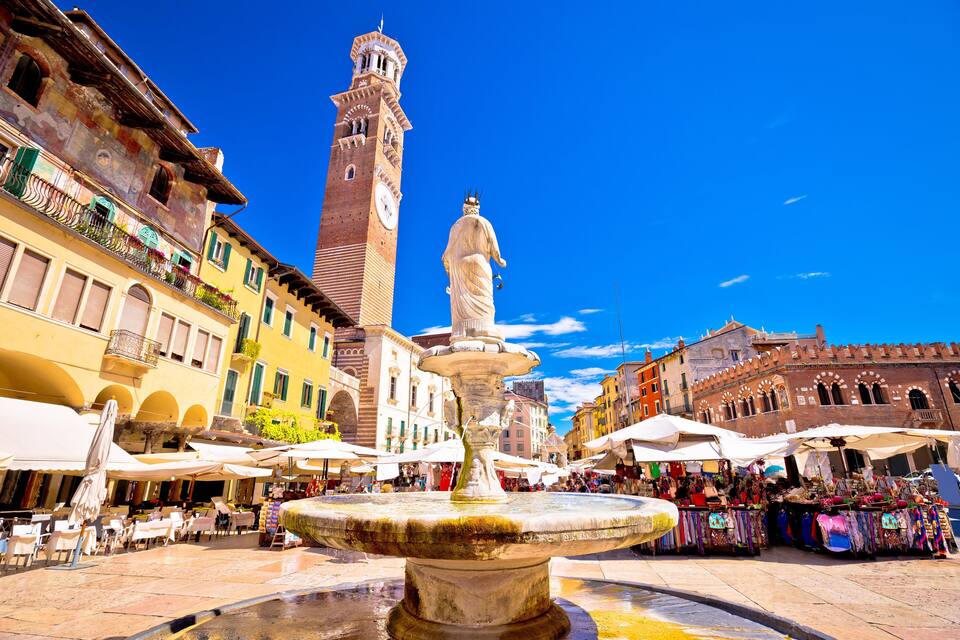 Une place historique agrémentée d’une fontaine, d’une tour horloge et de stands de marché.