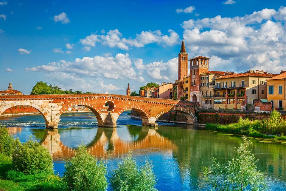 A stone bridge over a river with a tower and buildings in the background.