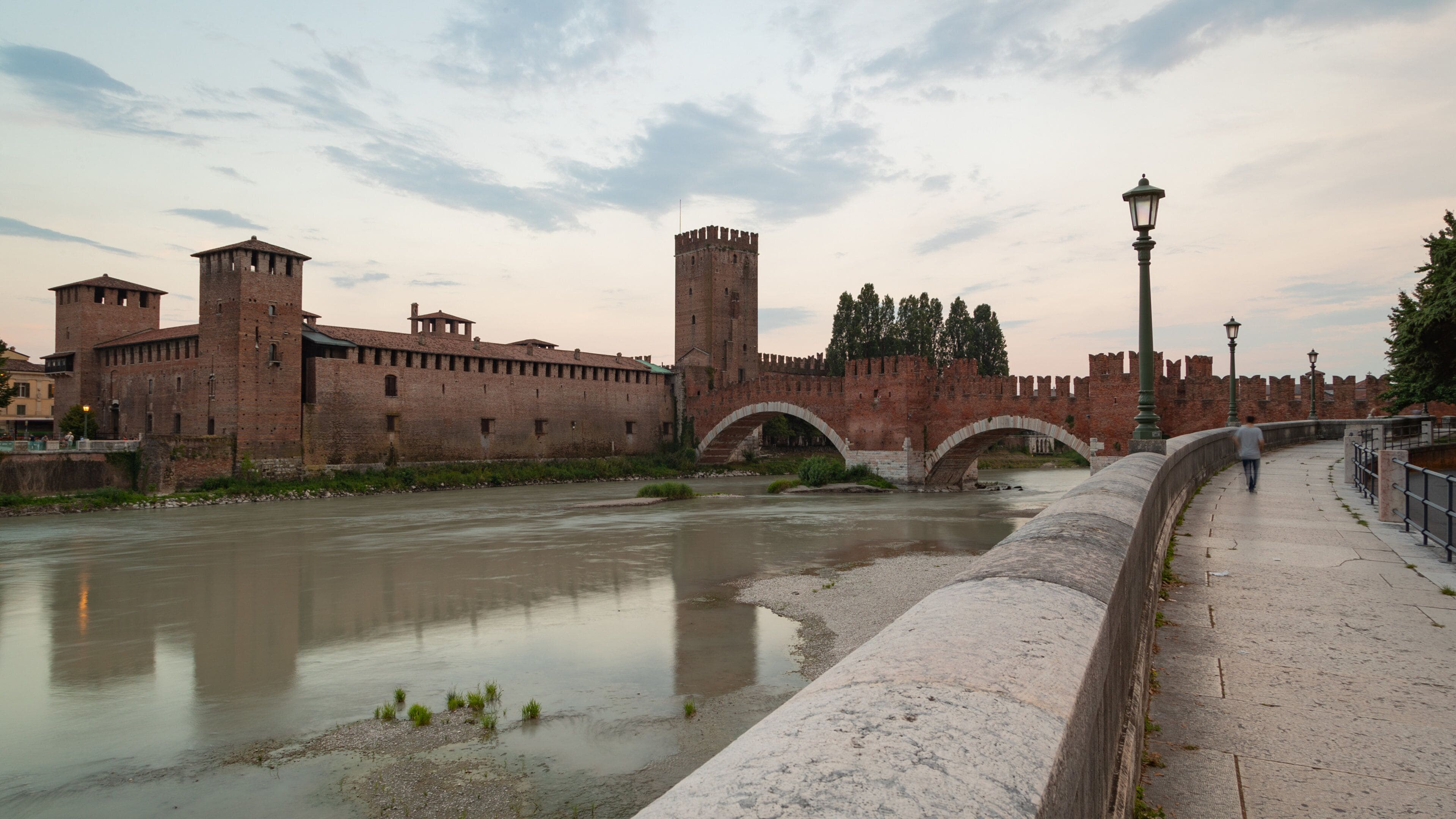 A historic stone bridge over a river, surrounded by medieval fortifications and a paved walkway.
