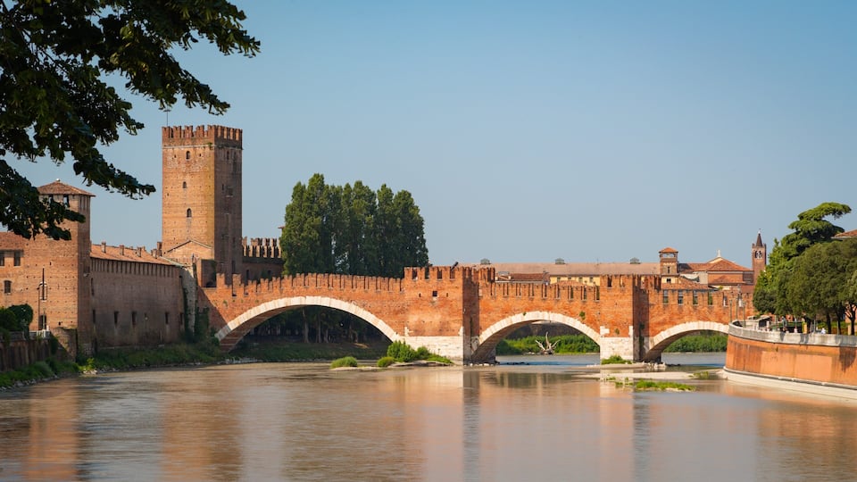 A historic stone bridge over a river, with a castle and tower in the background.