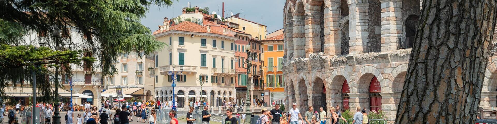 A bustling square with historic stone arches, a variety of colorful buildings, and people walking around.