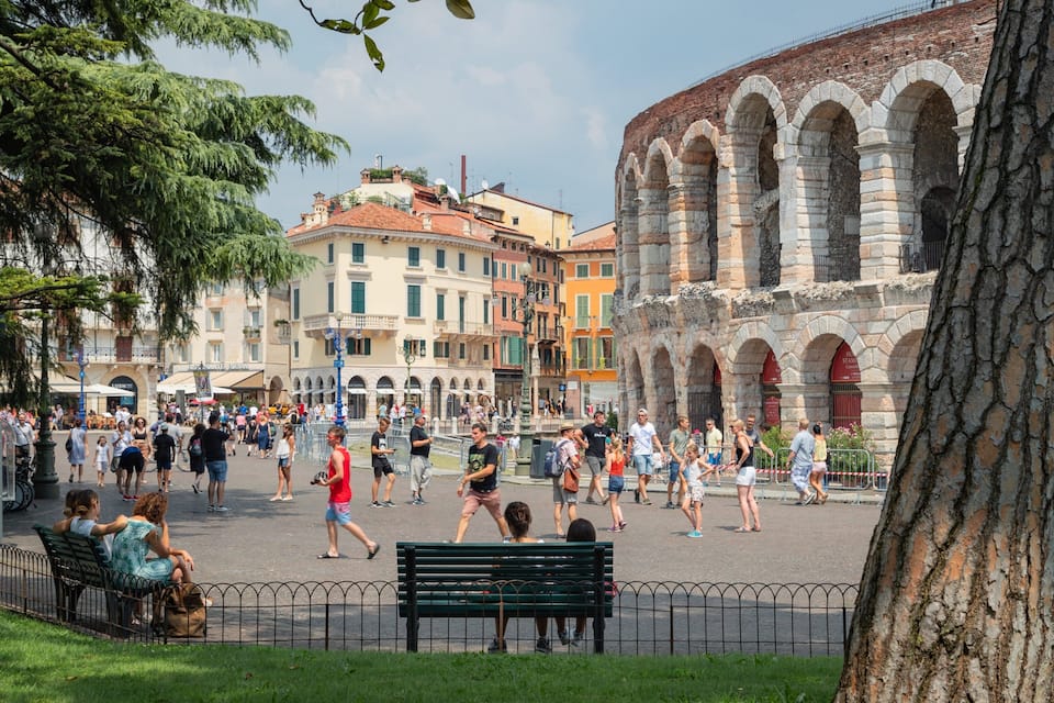 A bustling square with historic stone arches, a variety of colorful buildings, and people walking around.