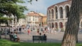 A bustling square with historic stone arches, a variety of colorful buildings, and people walking around.