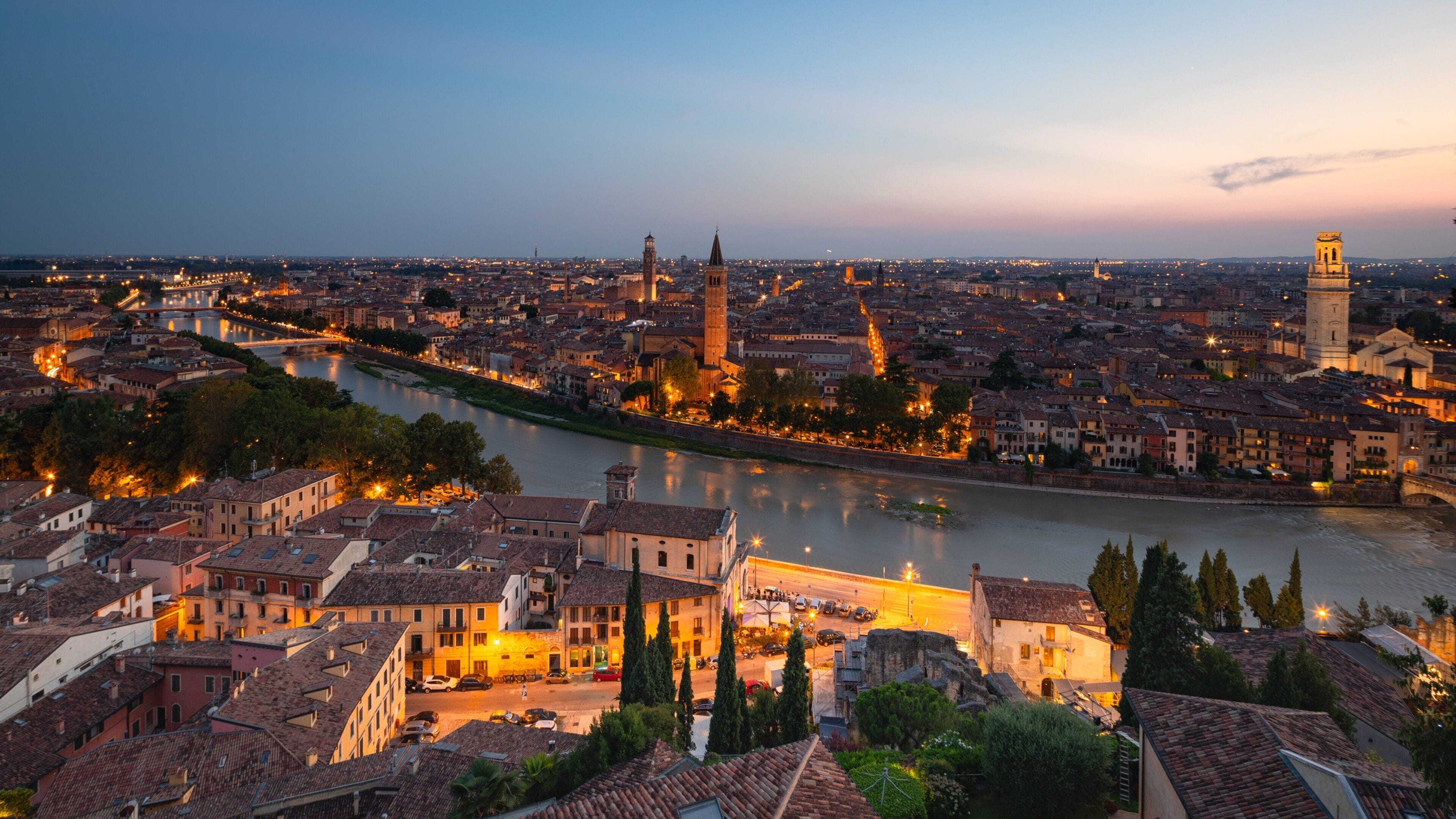 A panoramic view of a city at dusk with a river, historic buildings, and a prominent tower.