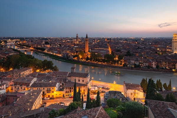 A panoramic view of a city at dusk with a river, historic buildings, and a prominent tower.