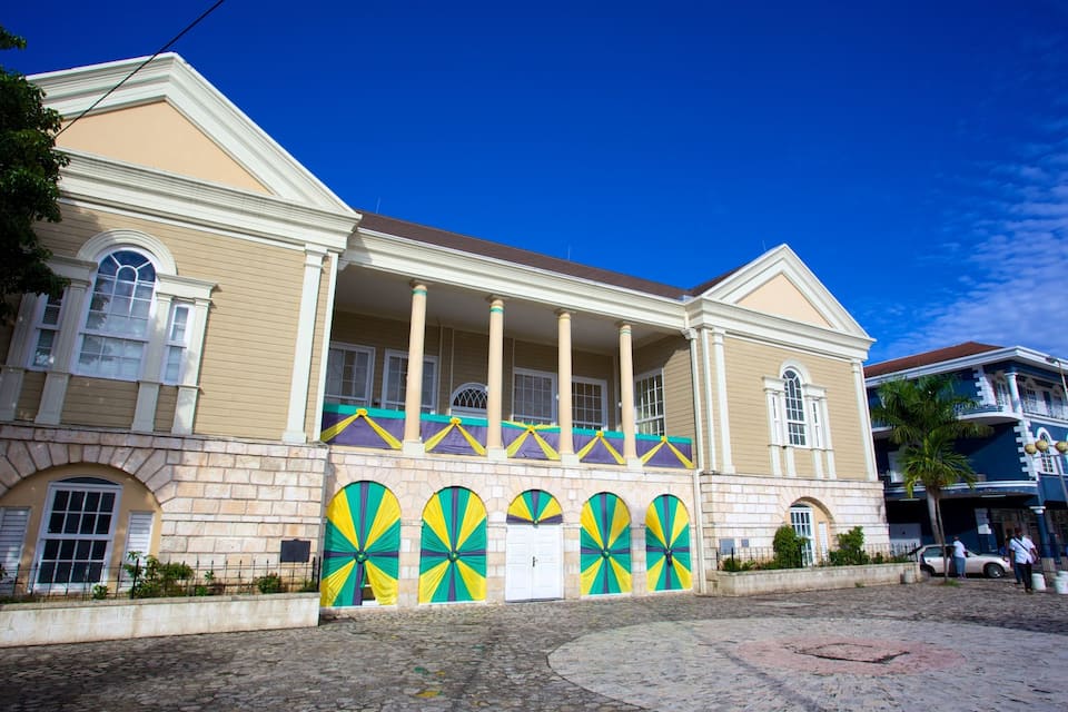 A historic building with colonial architecture, featuring a balcony with columns and colorful drapery.