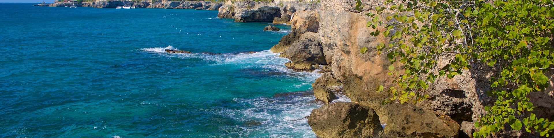 A coastal landscape with rocky cliffs, clear blue waters, and buildings on the shore.