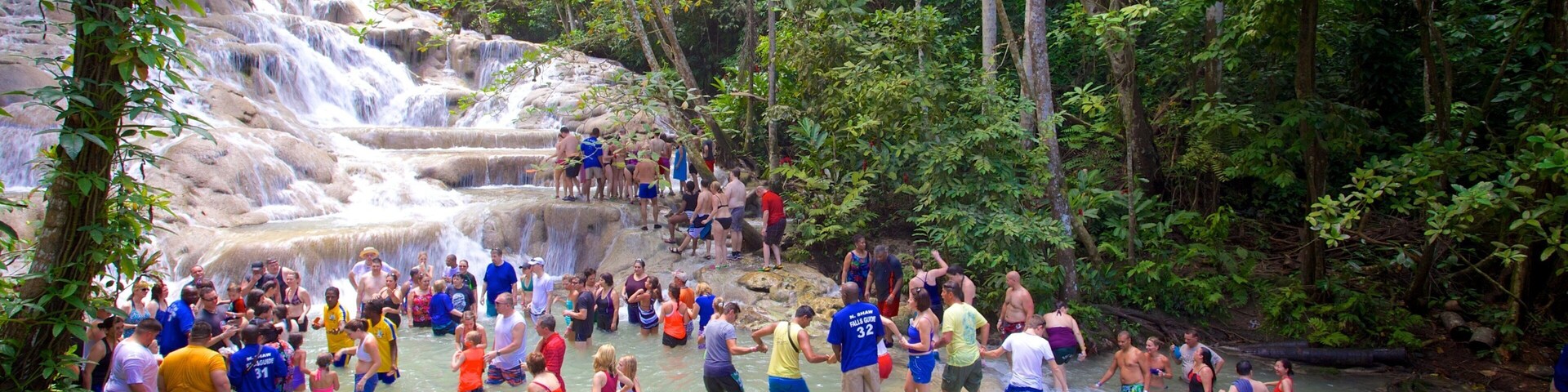 Una cascada en un área boscosa con gente disfrutando del agua.