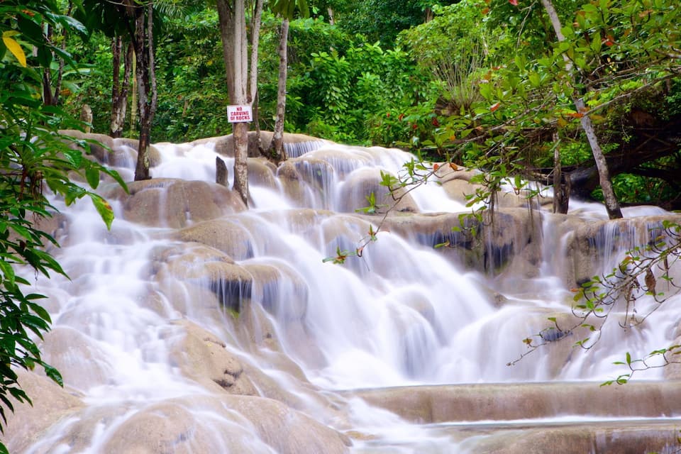 A waterfall cascading over rocks in a forested area with a 'No Carving of Rocks' sign.