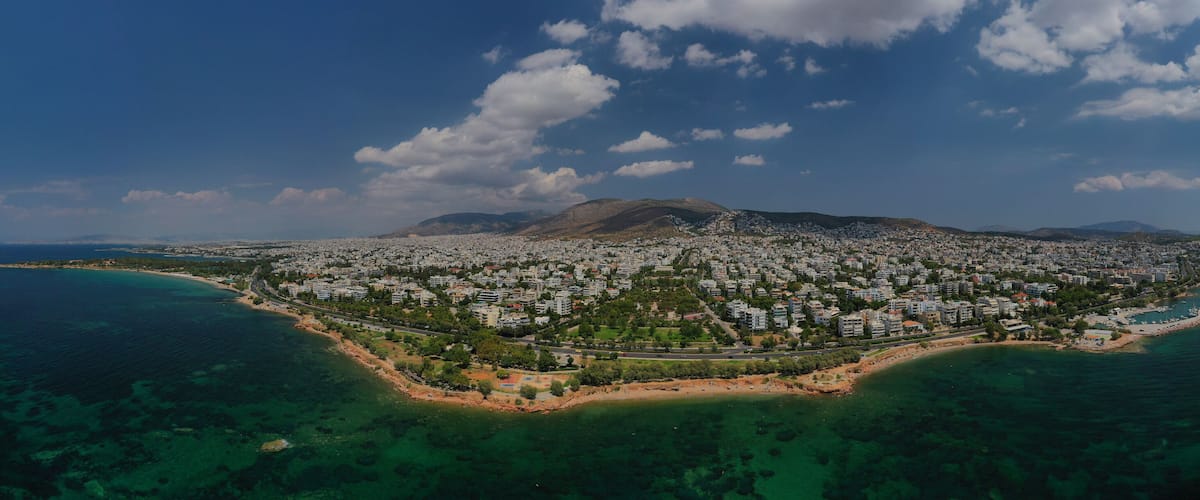 An aerial view of a coastal city with a mountain in the background, surrounded by clear blue waters and a densely populated urban area.