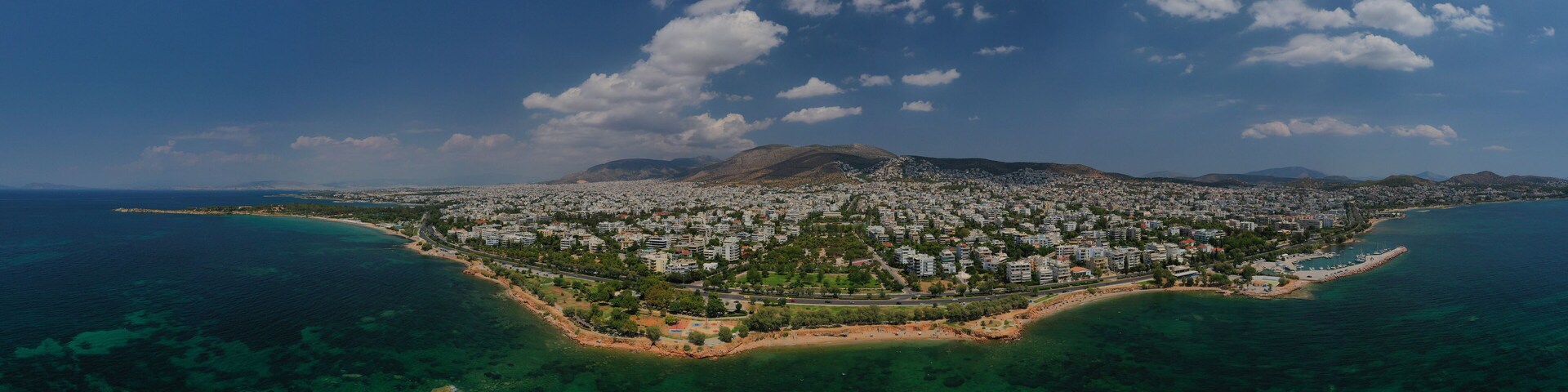 An aerial view of a coastal city with a mountain in the background, surrounded by clear blue waters and a densely populated urban area.