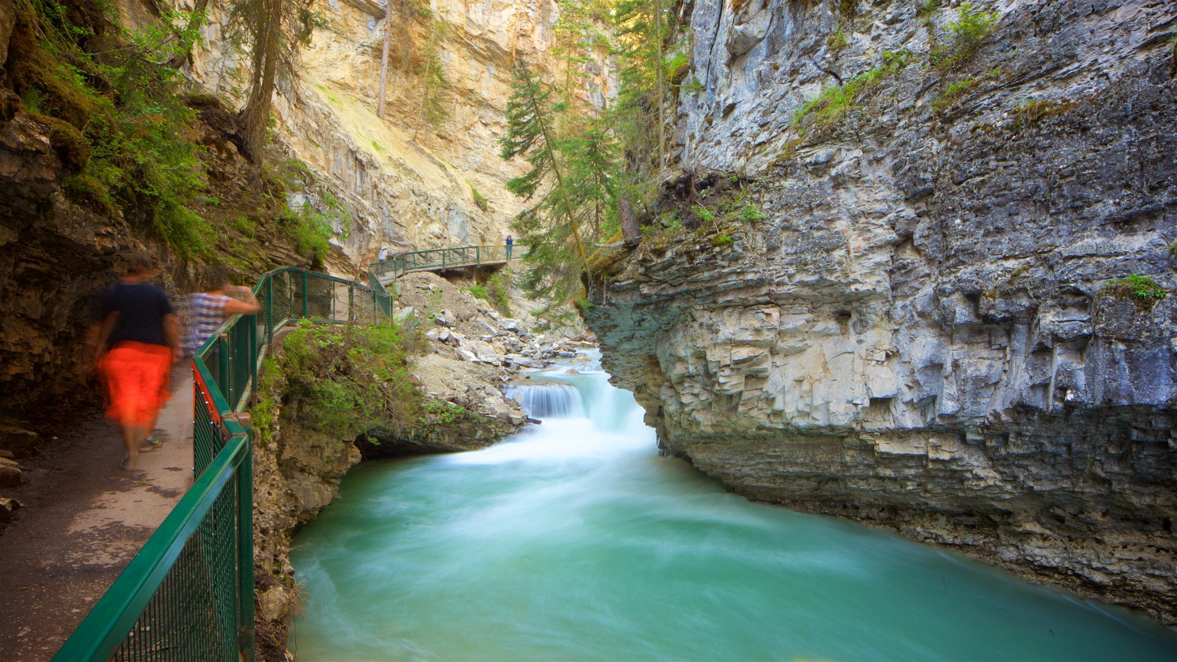 A waterfall in a rocky gorge with a bridge and a path.