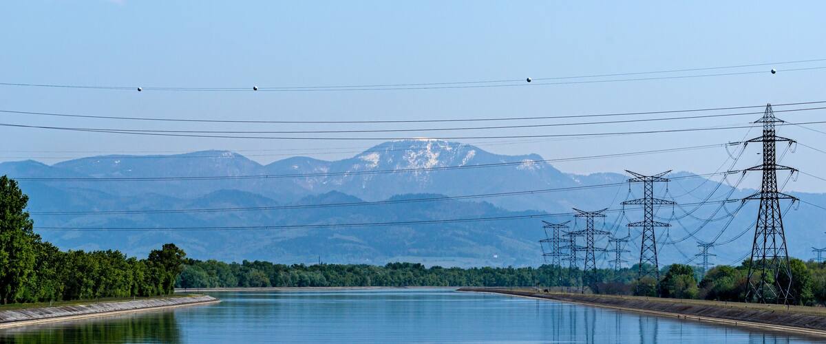 A calm river with mountains in the background and power lines running parallel to the water.