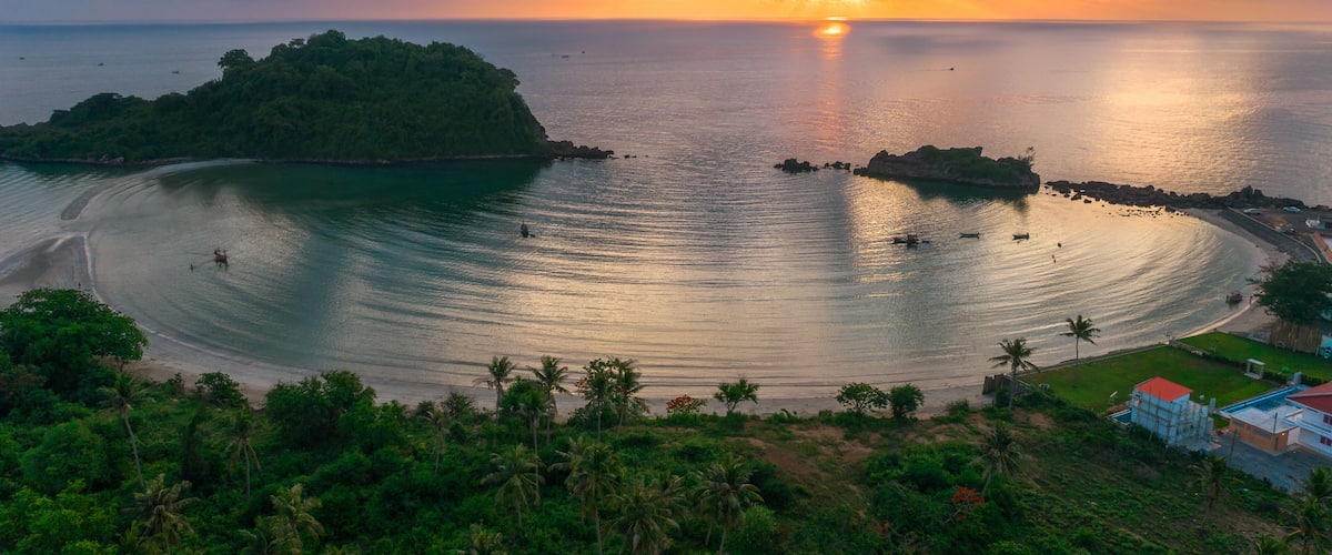 A tropical island at sunset with calm waters, a sandy beach, and lush greenery.