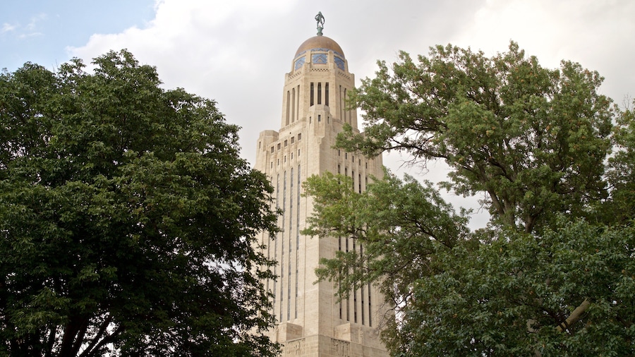Un edificio alto e histórico con una cúpula y una estatua en la parte superior, rodeado de frondosos árboles verdes.