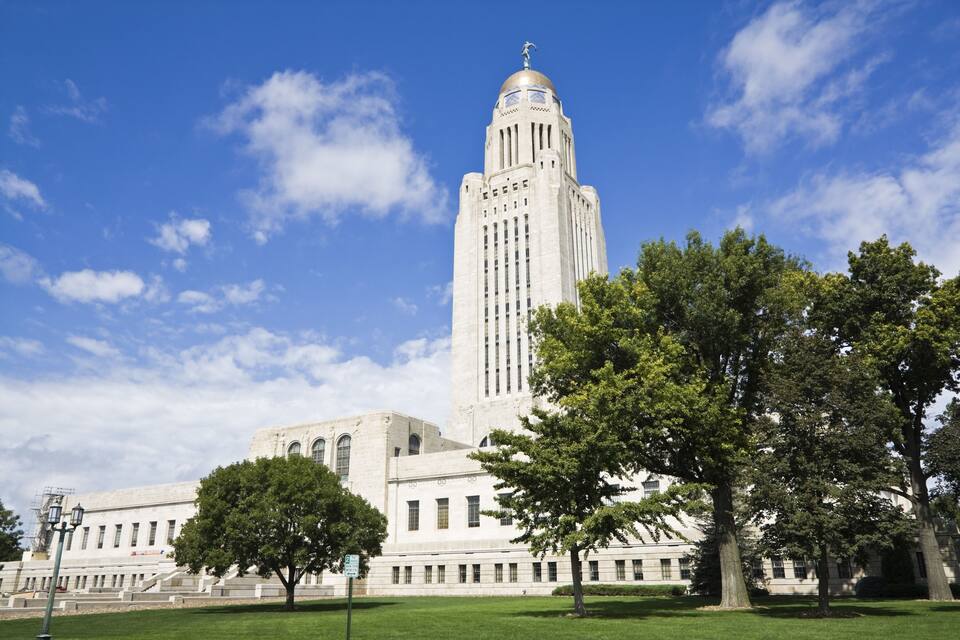 A large white building with a tall tower and a dome, surrounded by green grass and trees.