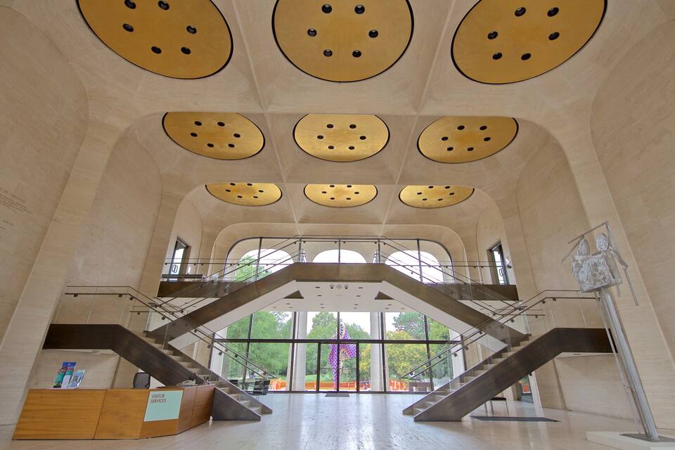 A modern building interior with a central staircase, large circular ceiling decorations, and a visitor services desk.