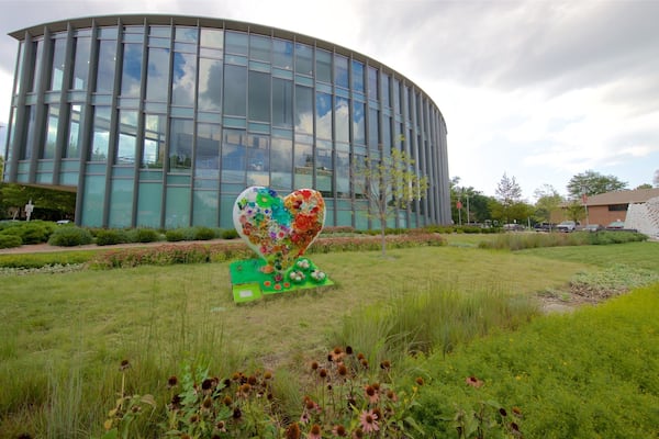 En moderne bygning med en glasfacade, en hjerteformet skulptur i en græsplæne og et træ i forgrunden.