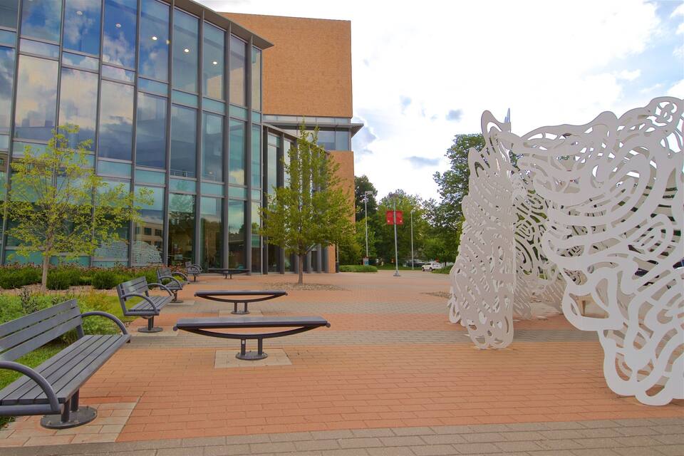 A modern building with glass windows, outdoor benches, and a decorative white structure.