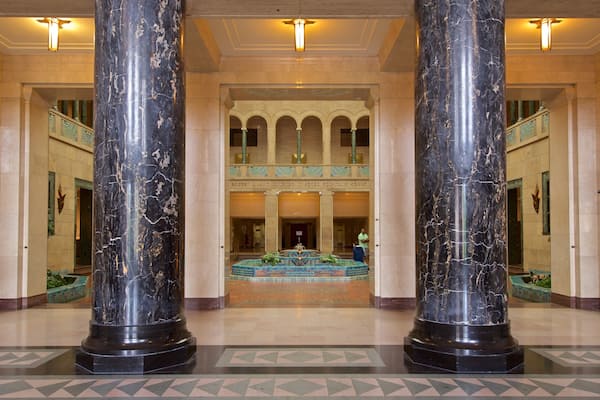 A grand lobby with large black marble columns, a central fountain, and a patterned floor.