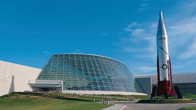 Un edificio moderno con fachada de vidrio y un gran cohete en exhibición.