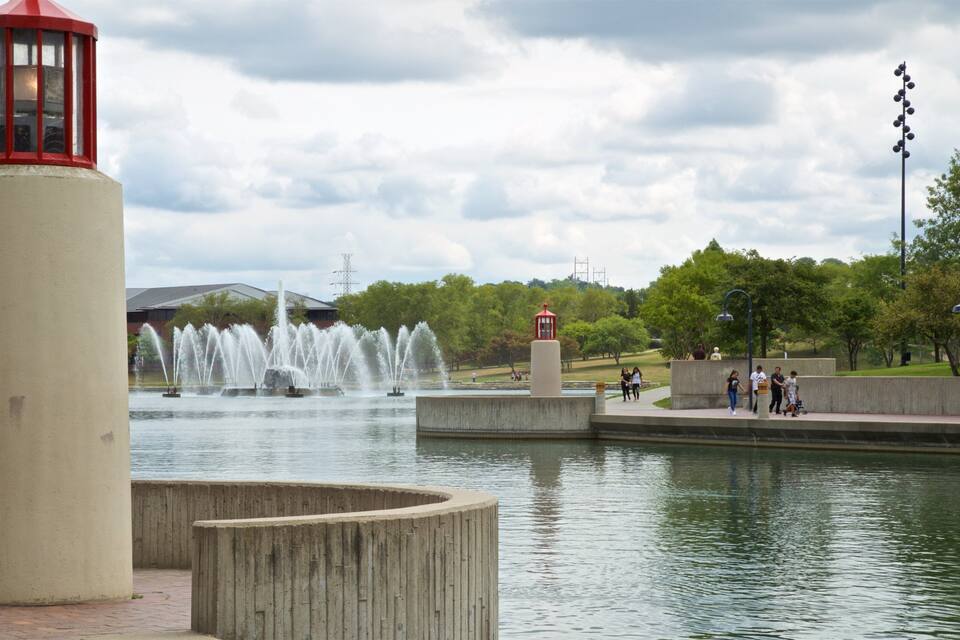 Um parque com uma fonte de água, uma estrutura semelhante a um farol vermelho e um muro de concreto.