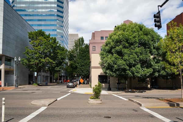 A city intersection with modern buildings, trees, and a traffic light.
