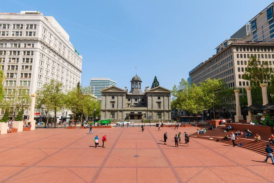 Uma praça com um edifício central com cúpula e colunas, rodeada por edifícios altos e modernos.
